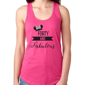 Pode incluir: Camisola de al&ccedil;as rosa com um gr&aacute;fico preto e branco que diz "Forty and Fabulous" com orelhas de Mickey Mouse de glitter prateado e um la&ccedil;o no topo.