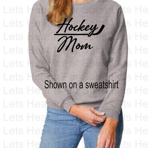 K&ouml;nnte beinhalten: Ein graues Sweatshirt mit dem Text "Hockey Mom" in schwarzen Buchstaben. Der Text ist mit einem Hockeyschl&auml;ger durch das Wort "Mom" stilisiert.