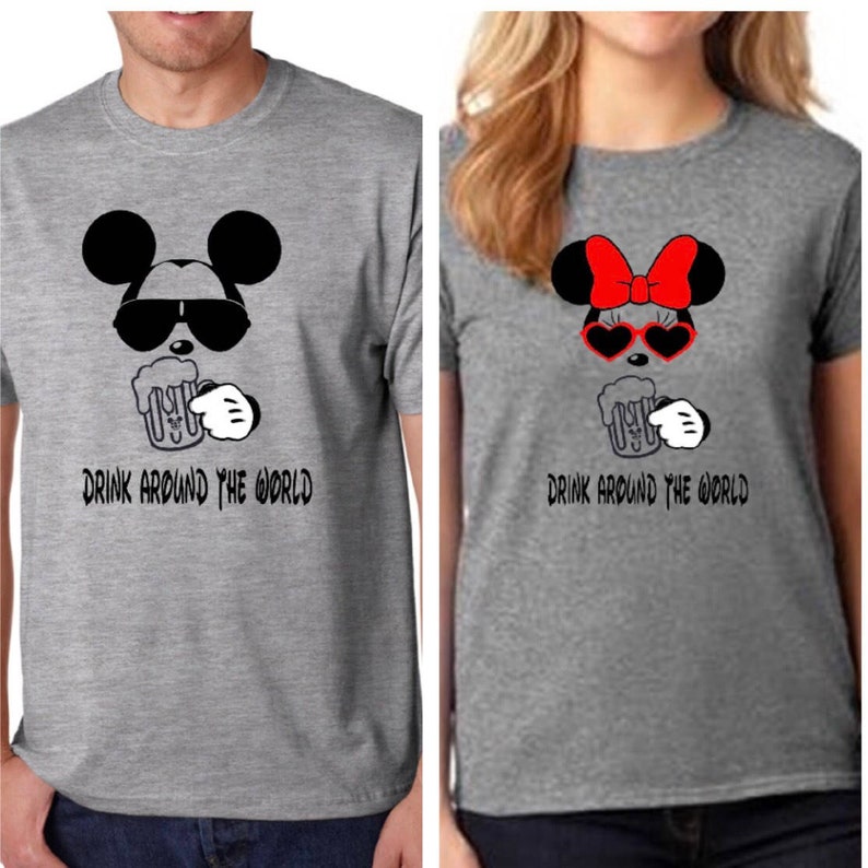 Peut inclure: Deux t-shirts gris avec des graphiques de dessins anim&eacute;s assortis. L'un repr&eacute;sente Mickey Mouse avec des lunettes de soleil tenant une chope de bi&egrave;re, l'autre Minnie Mouse avec un n&oelig;ud rouge et des lunettes de soleil en forme de c&oelig;ur. Le texte "DRINK AROUND THE WORLD" est imprim&eacute; en dessous.