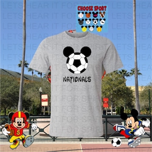 May include: A gray t-shirt featuring a soccer ball design with Mickey Mouse ears and the word "NATIONALS" in black. Additional sports-themed Mickey Mouse designs are displayed above the shirt.