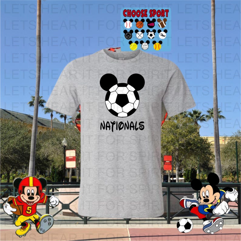 May include: A gray t-shirt featuring a soccer ball design with Mickey Mouse ears and the word "NATIONALS" in black. Additional sports-themed Mickey Mouse designs are displayed above the shirt.