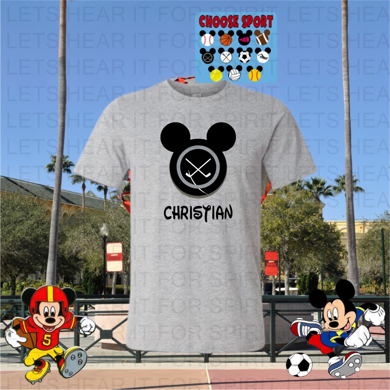 May include: A light gray t-shirt featuring a black Mickey Mouse head with crossed hockey sticks inside a circle. The name "CHRISTIAN" is printed below. Additional sports-themed Mickey Mouse designs are displayed above.