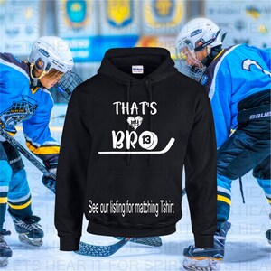 K&ouml;nnte beinhalten: Schwarzer Kapuzenpullover mit wei&szlig;em Text, der "That's my BRO 13" lautet, mit einem Grafikmotiv aus Hockeyschl&auml;ger und Puck. Siehe unsere Liste f&uuml;r das passende T-Shirt.