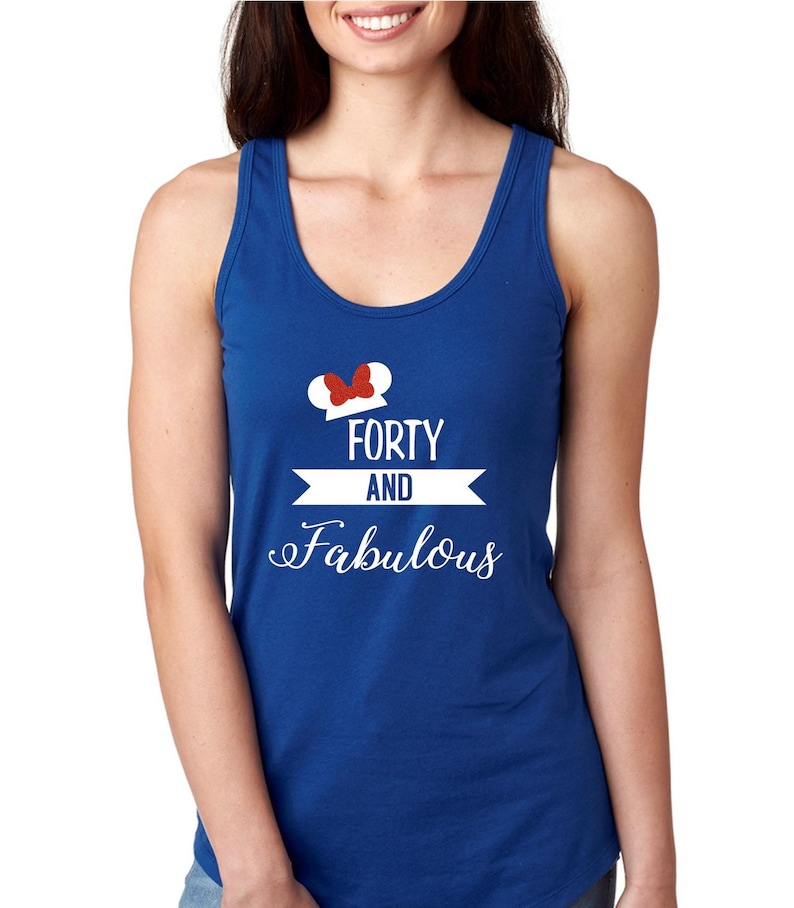 Pode incluir: Um top de al&ccedil;as azul royal com um gr&aacute;fico branco que diz "Forty and Fabulous" com um la&ccedil;o vermelho no topo de uma silhueta de orelha do Mickey Mouse branca.