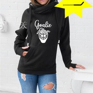 K&ouml;nnte beinhalten: Schwarzer Hoodie mit einem wei&szlig;en Aufdruck eines Hockeytorwart-Masken und dem Text "Goalie Mom". Der Hoodie hat einen Kapuzenkragen und eine Tasche auf der Vorderseite.