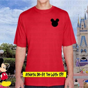 May include: Red athletic dri-fit tee shirt with a black Mickey Mouse head logo. The shirt has the text "Athletic Dri-fit Tee With SPF" in yellow. The shirt is short-sleeved.