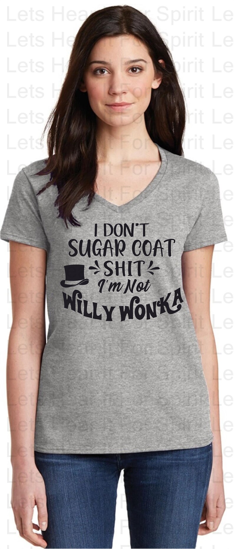 May include: A grey V-neck t-shirt with the text "I DON'T SUGAR COAT SHIT I'M NOT WILLY WONKA" in black. The shirt features a top hat graphic. The model is wearing blue jeans.