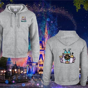 May include: A grey zip-up hoodie with a small world graphic on the front and a cartoon illustration of a castle on the back. The hoodie is in front of a blurred background of a nighttime amusement park.