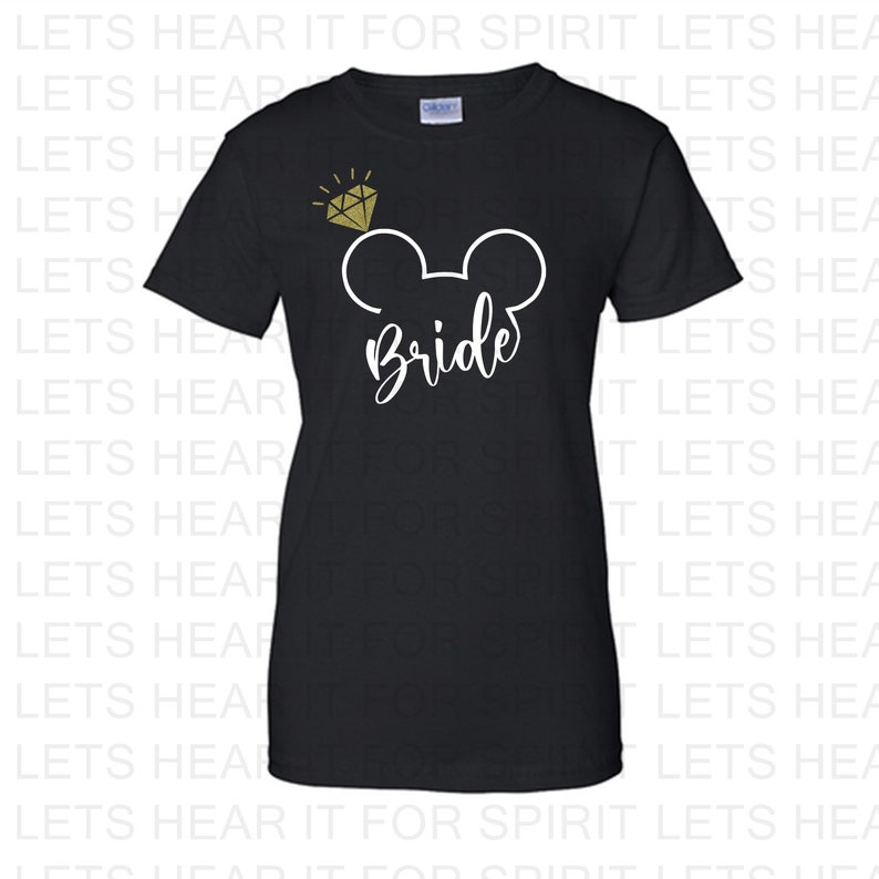 May include: Black t-shirt featuring a white Mickey Mouse head design with a gold glitter diamond above it. The text "Bride" is written in white below the Mickey Mouse head.
