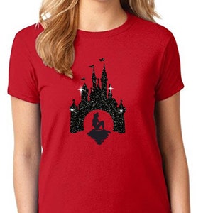 Puede incluir: Camiseta roja con un dise&ntilde;o de purpurina negra de una silueta de castillo y una sirena frente a una luna llena. La camiseta tiene cuello redondo y est&aacute; hecha de un material suave.