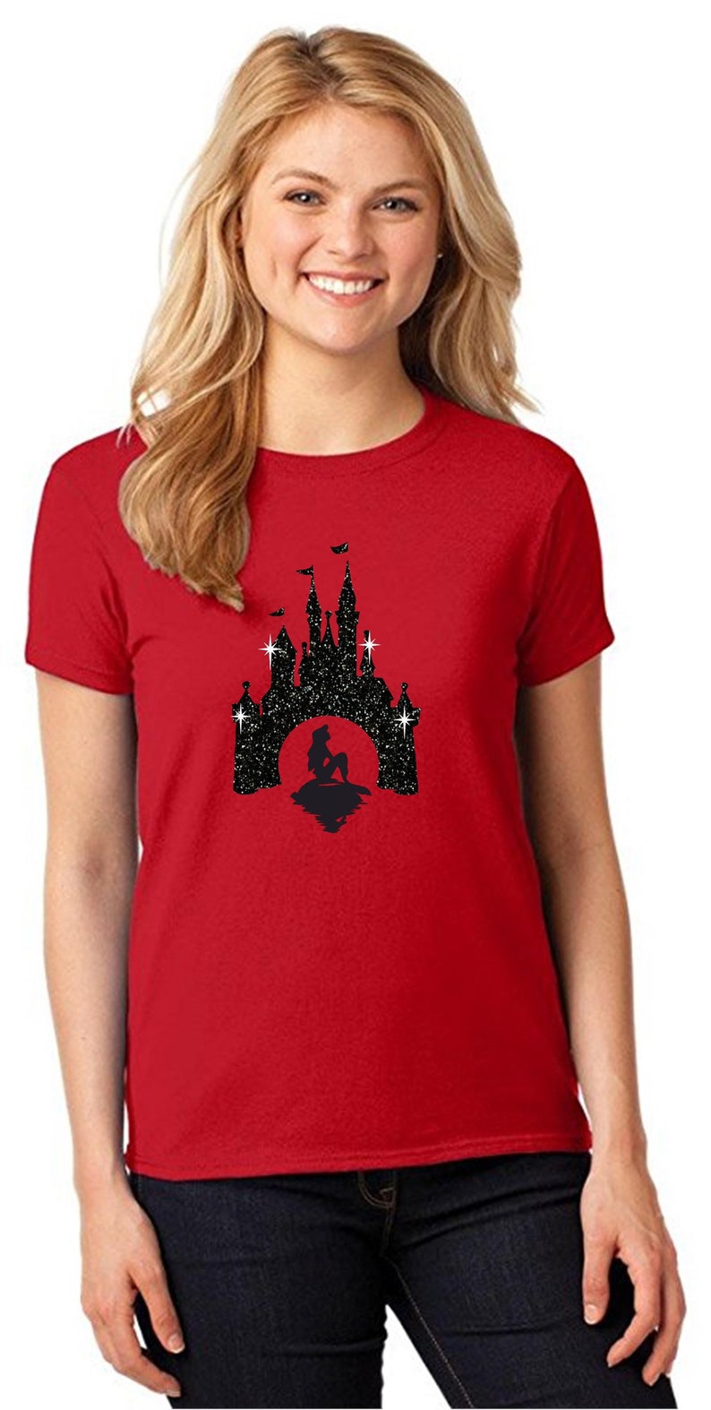 Puede incluir: Camiseta roja con un dise&ntilde;o de purpurina negra de una silueta de castillo y una sirena frente a una luna llena. La camiseta tiene cuello redondo y est&aacute; hecha de un material suave.