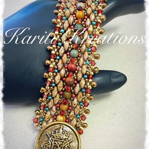 Könnte beinhalten: Ein Armband aus Perlen mit einem goldenen Knopf, der eine Krone und ein Wappen zeigt. Das Armband besteht aus braunen, weißen, roten, orangefarbenen, grünen und blauen Perlen.