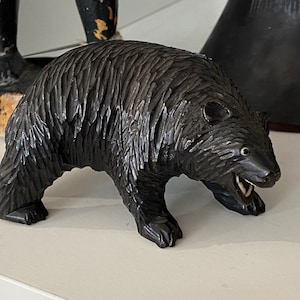 May include: A black wooden carving of a bear with its mouth open, showing its teeth. The bear is standing on all fours and has a detailed fur texture.