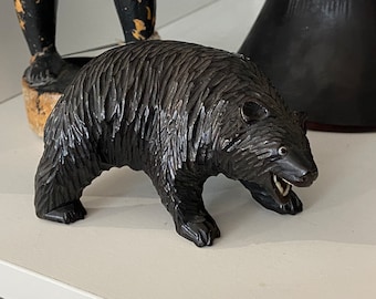 May include: A black wooden carving of a bear with its mouth open, showing its teeth. The bear is standing on all fours and has a detailed fur texture.