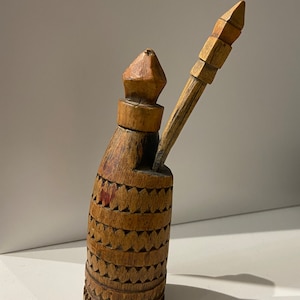 May include: A wooden bottle with a carved design and a wooden stopper. The bottle has a long, thin spout and a small, round base. The stopper is shaped like a cone and has a small, round knob on top.