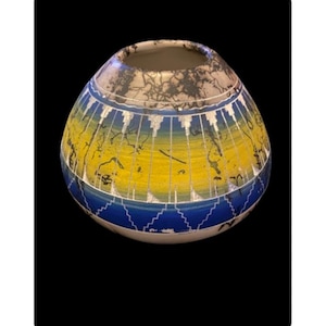 May include: A round, white ceramic pot with a blue and yellow geometric design. The pot has a black and white pattern on the top.