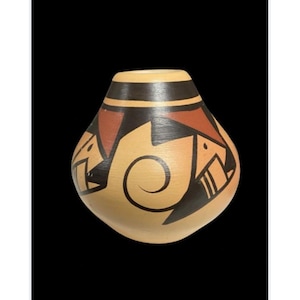 Puede incluir: Un pequeño jarrón de cerámica pintado a mano con un diseño geométrico marrón, negro y rojo. El jarrón tiene un cuerpo redondeado y un cuello estrecho.