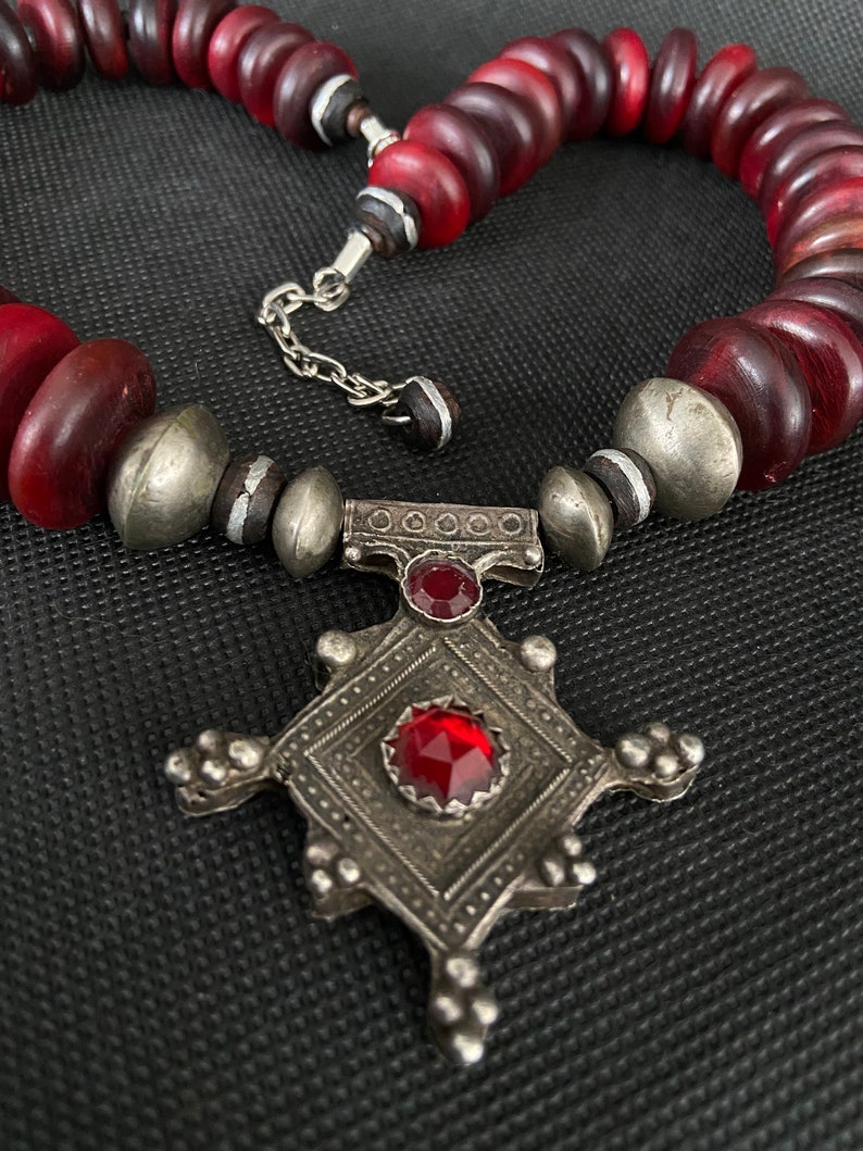 May include: A red glass bead necklace with a silver pendant featuring a cross design and red gemstones.