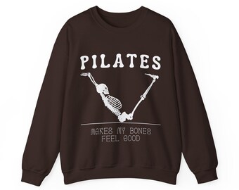 May include: A brown sweatshirt with the text "PILATES makes my bones feel good" and a white skeleton doing a pilates pose.