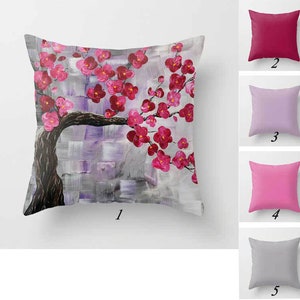 May include: A throw pillow with a pink and gray floral design. The pillow features a stylized painting of a tree with pink blossoms. The pillow is shown against a white background.