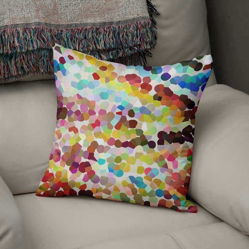 May include: A square throw pillow featuring a vibrant, multi-colored mosaic pattern of small, rounded shapes in shades of red, yellow, blue, green, and purple against a white background, creating a dense, abstract, and colorful pointillist design.