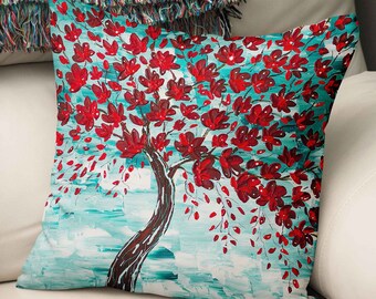 May include: A square throw pillow featuring a painted tree with a dark brown trunk and branches covered in vibrant red blossoms. The background consists of textured brushstrokes in shades of light blue, turquoise, and white, creating a dynamic effect.