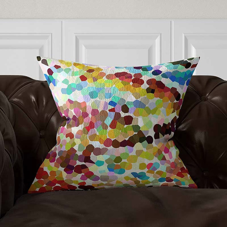 May include: A square throw pillow featuring a vibrant, multi-colored mosaic pattern of small, rounded shapes in shades of red, yellow, blue, green, and purple against a white background, creating a dense, textured, and colorful visual effect.
