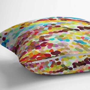 May include: A square throw pillow featuring a vibrant, multi-colored mosaic pattern of small, rounded shapes in shades of red, yellow, blue, green, and purple against a white background, complete with a white zipper closure along the bottom edge.