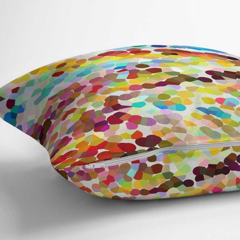 May include: A square throw pillow featuring a vibrant, multi-colored mosaic pattern of small, rounded shapes in shades of red, yellow, blue, green, and purple against a white background, complete with a white zipper closure along the bottom edge.