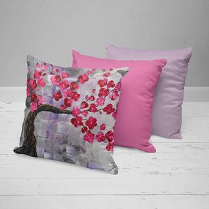 May include: Two decorative throw pillows, one with a pink floral design and the other a solid pink color. The floral pillow features a gray background with a stylized pink cherry blossom branch.