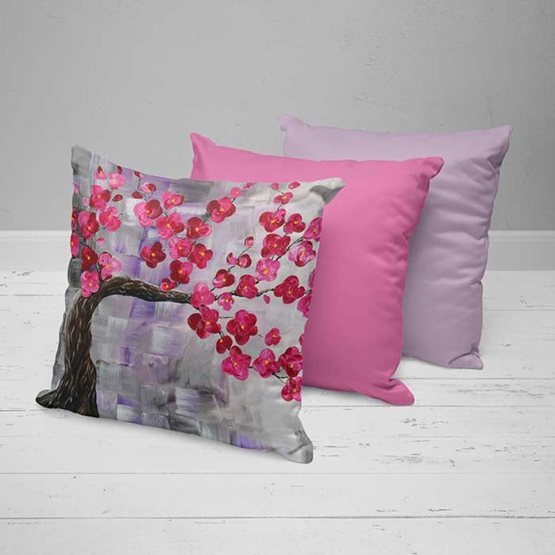 May include: Two decorative throw pillows, one with a pink floral design and the other a solid pink color. The floral pillow features a gray background with a stylized pink cherry blossom branch.