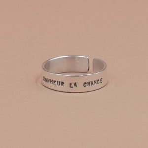 Puede incluir: Un anillo de plata con la inscripción "BONHEUR LA CHANCE" en la banda.