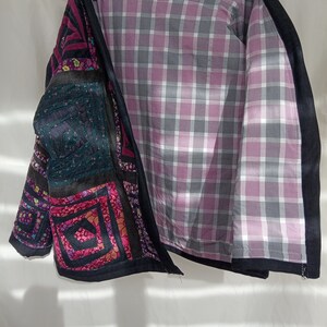 May include: A black quilted jacket with a patchwork design featuring various colors and patterns, including pink, green, and brown. The jacket is lined with a pink and gray plaid fabric.