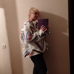 May include: A quilted jacket with a patchwork design in white, blue, red, and yellow. The jacket has a relaxed fit and is paired with black jeans and white sneakers. The overall style is casual and comfortable.
