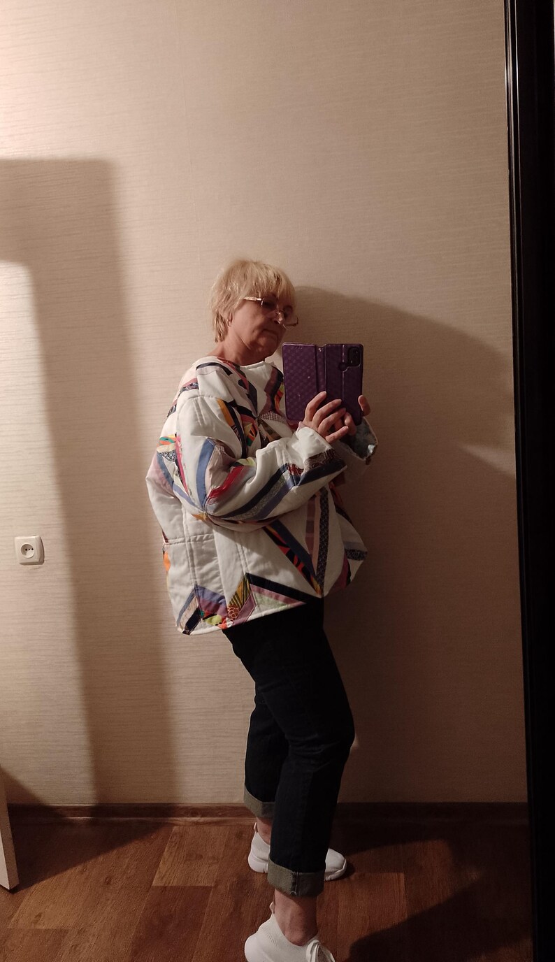 May include: A quilted jacket with a patchwork design in white, blue, red, and yellow. The jacket has a relaxed fit and is paired with black jeans and white sneakers. The overall style is casual and comfortable.