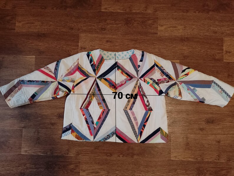 May include: A quilted jacket with a geometric design. The jacket is white with colorful fabric strips arranged in diamond and starburst patterns. The jacket measures 70 cm across.