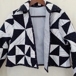 Puede incluir: Una chaqueta acolchada en blanco y negro con un patrón geométrico. La chaqueta tiene cuello y cierre de botones.