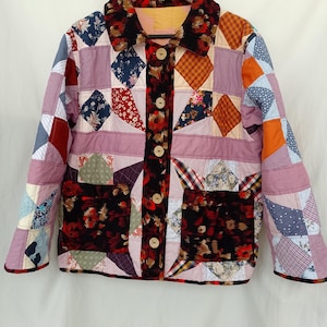 Könnte beinhalten: Eine gesteppte Jacke mit einem Patchwork-Design aus verschiedenen Stoffmustern, darunter Blumen, Karos und unifarbene Stoffe. Die Jacke hat einen dunklen, geblümten Samtkragen, passende Samttaschen auf der Vorderseite und fünf helle Holzknöpfe.