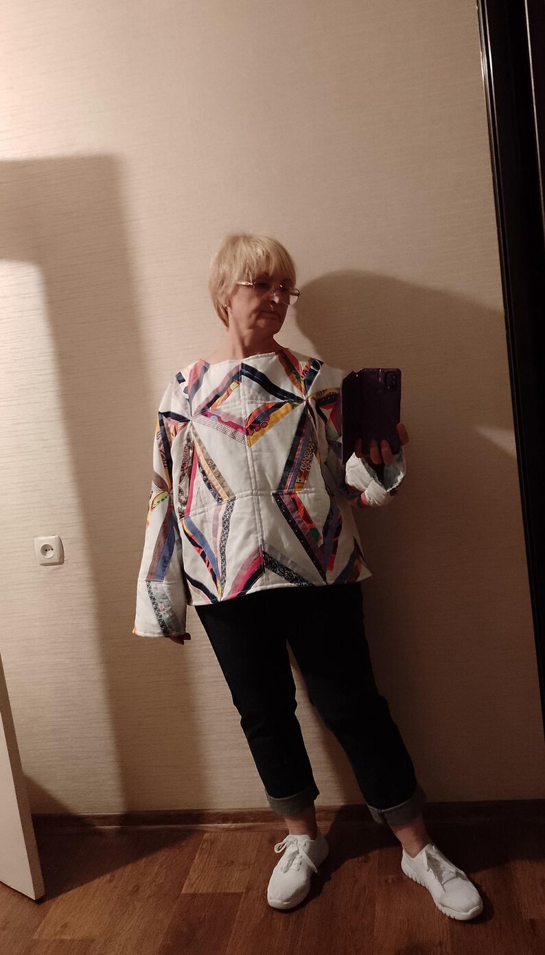 May include: A white patchwork top with geometric patterns in various colors, including red, blue, and yellow. The top is paired with black pants and white sneakers. The overall style is casual and handmade.
