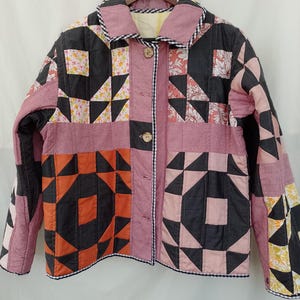 May include: A long-sleeve jacket constructed from a patchwork of quilted fabric squares in shades of pink, black, orange, and floral patterns. The jacket features a collared neckline, a front button closure with wooden buttons, and black and white gingham trim.