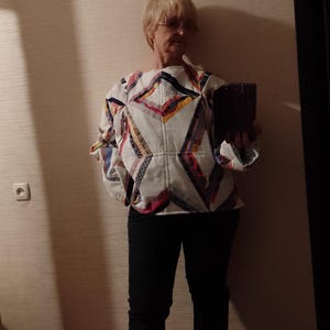 May include: A white quilted top with a geometric patchwork design in various colors, paired with dark blue jeans and white sneakers. The top features a unique, handcrafted aesthetic, showcasing a blend of textures and patterns.