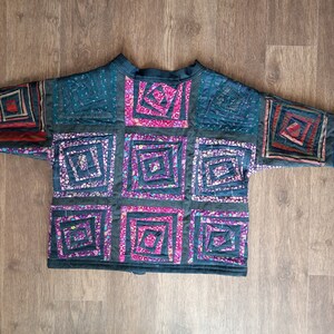 May include: A dark blue quilted jacket with a patchwork design. The patches are made of different fabrics and colors, including pink, purple, and blue. The jacket has a stand-up collar and a zipper closure.