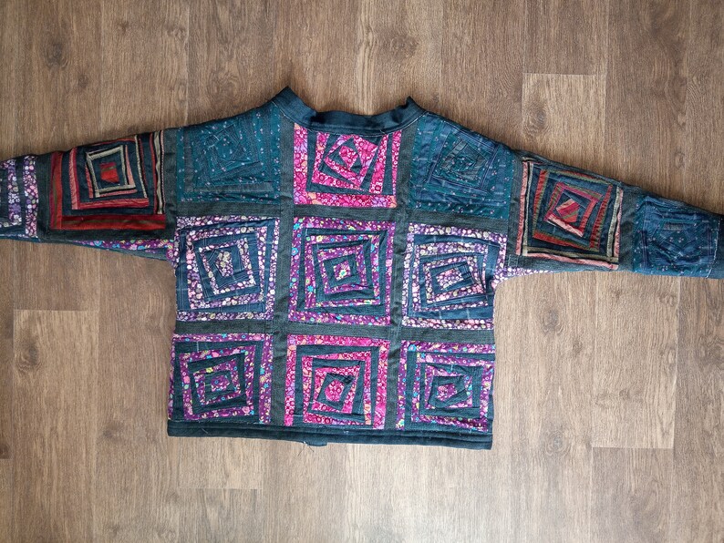 May include: A dark blue quilted jacket with a patchwork design. The patches are made of different fabrics and colors, including pink, purple, and blue. The jacket has a stand-up collar and a zipper closure.