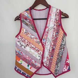 Pode incluir: Um colete sem mangas feito de tecido patchwork. O colete é uma mistura de tecidos rosa, laranja, branco e marrom com padrões florais e geométricos. O colete tem um decote em V e é forrado com um tecido rosa.