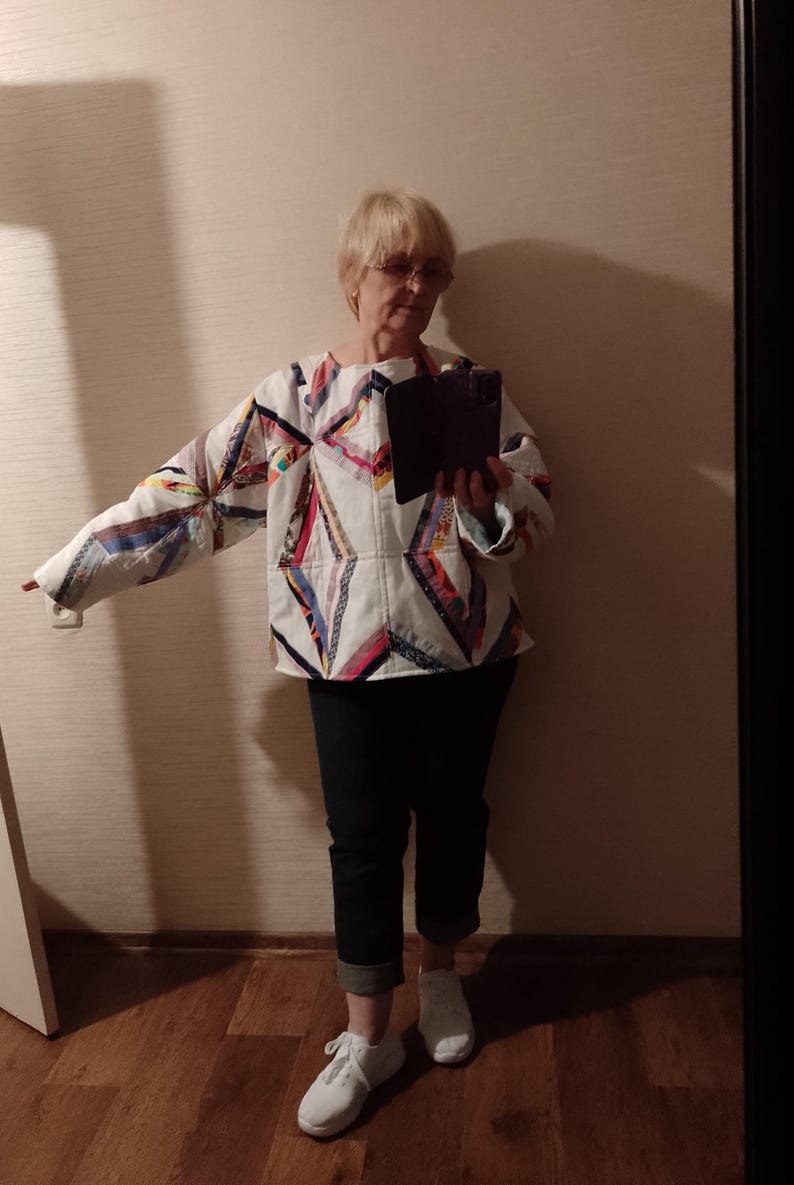 May include: A quilted jacket with a geometric pattern in various colors, including red, blue, and yellow, is paired with dark blue jeans and white sneakers. The jacket's design features a patchwork style.