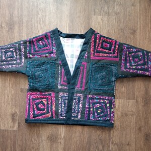 May include: A black quilted jacket with a V-neck and a patchwork design featuring squares of different floral patterns in shades of pink, purple, and green.