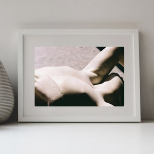 Könnte beinhalten: Ein gerahmter Druck mit einer klassischen Skulptur einer menschlichen Form. Das Kunstwerk befindet sich in einem weißen Rahmen und ruht auf einer weißen Oberfläche. Die Skulptur ist hellbeige, mit sichtbaren Details und Schatten.