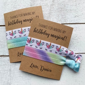 May include: Two brown cards with the text "Thanks for making my birthday magical!" and "Love, Danica" with a unicorn hair tie attached to each card.