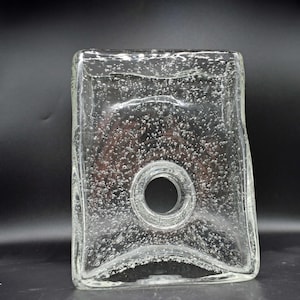 May include: A clear glass vase with a rectangular shape and a central circular opening. The glass features a distinct bubble texture throughout the body, creating a porous appearance. The edges are slightly curved, and the surface is smooth.