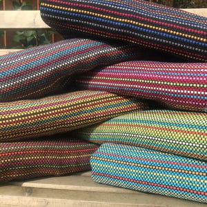 Puede incluir: Una pila de objetos cilíndricos tejidos y coloridos. Cada objeto presenta un patrón repetitivo de rayas horizontales en varios colores, incluyendo azul, rojo, amarillo y verde. Los objetos están sobre una superficie de madera.